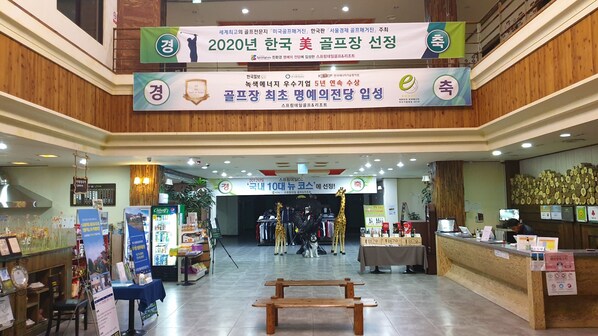 A spacious indoor area with a reception desk, a display of wine bottles, and a wooden bench in the center. - Springdale (Seogwipo)