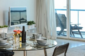 Mesa de comedor servida con platos, tazones, vasos y una botella, con vista a un balcón y una silla.