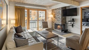 A cozy living room with a stone fireplace, a sofa, a coffee table, and a TV mounted on the wall.