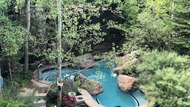 A hot tub surrounded by rocks and greenery, with a chair and table nearby.