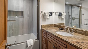 A modern bathroom with a large mirror, a bathtub, a shower, and a sink.