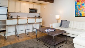 A modern living room with a white sofa, a coffee table, and a kitchen area with white cabinets and a microwave.