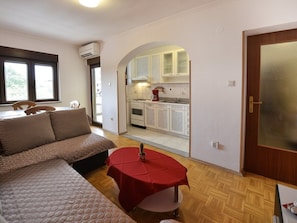 A compact living space with a sofa, a small dining table, and a kitchen area visible through an archway. - Apartment Kuki in Porec, Istria (Porec)