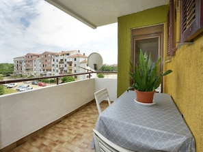A balcony with a table, chairs, a potted plant, a satellite dish, and a view of buildings in the background. - Apartment Kuki in Porec, Istria (Porec)