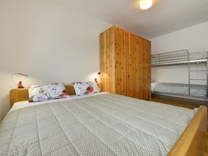 A bedroom with a large bed, a wooden headboard, a bunk bed, and a bedside table with a lamp. - Apartment Kuki in Porec, Istria (Porec)