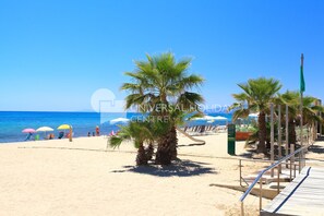 A beach with palm trees, umbrellas, and a wooden walkway.