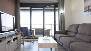 Una sala de estar moderna con un televisor de pantalla plana, un sofá, una butaca y una mesa de centro de vidrio.