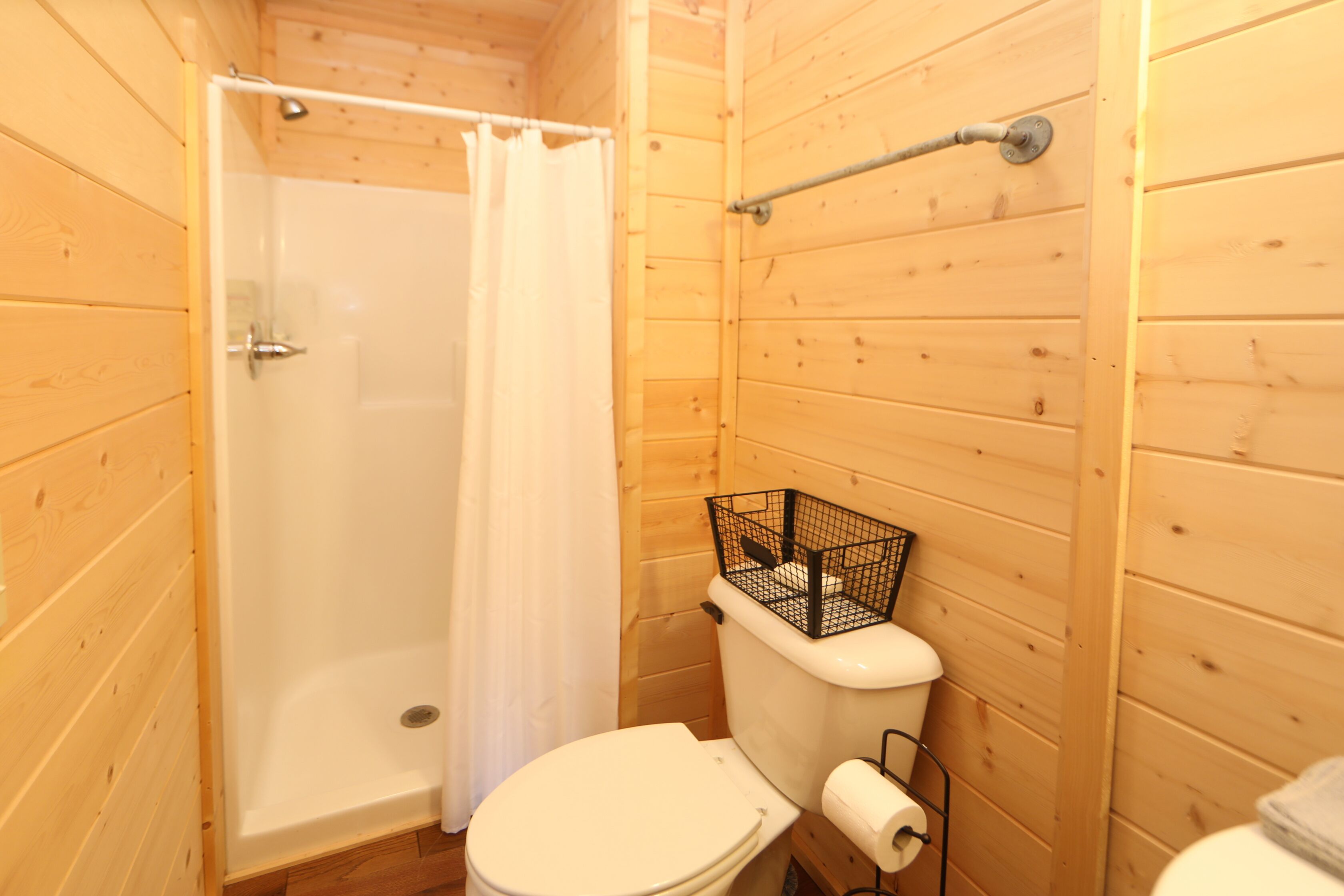 Un baño con paneles de madera, ducha, inodoro y un perchero para toallas.