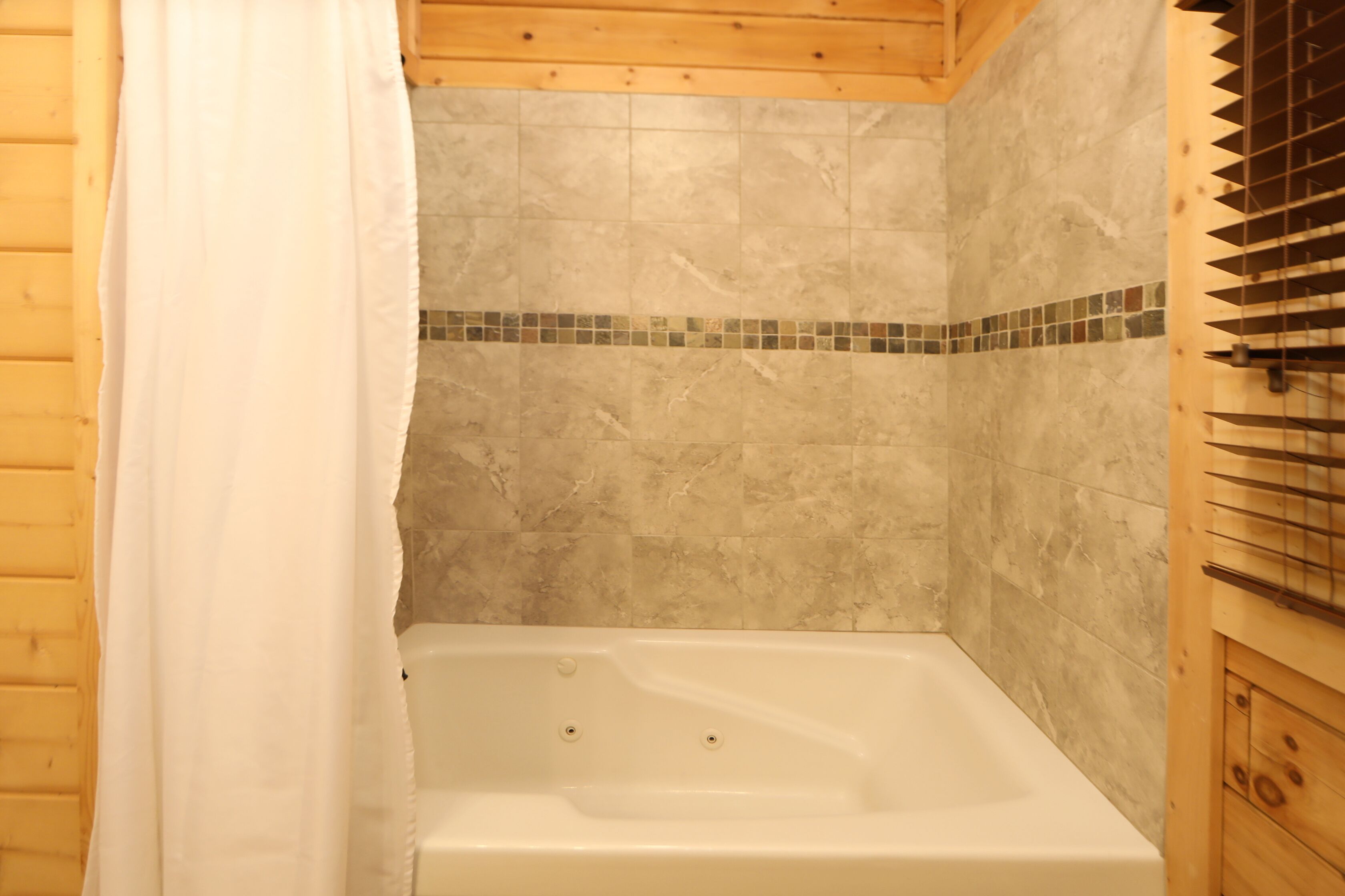 A bathroom with a bathtub, wooden ceiling, and tiled walls.