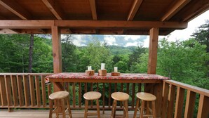 Um deck de madeira com uma mesa e quatro banquinhos, com vista para uma área arborizada.