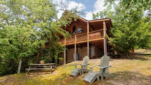 A wooden cabin with a balcony, surrounded by trees. - New Hot Tub, Beautiful Cabin, Resort Pool, Putt Putt, Golf, 5mi to Pigeon Forge (Sevierville)