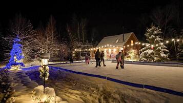 A snow-covered outdoor area with a wooden building, a blue-lit tree, and a snow-covered landscape.
