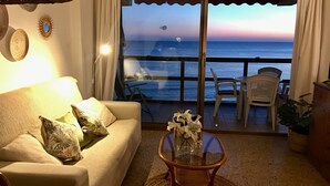 A living room with a sofa, a glass coffee table with flowers, and a view of the ocean at sunset. - A47 CALPEMAR C 5º 19 (Calpe)