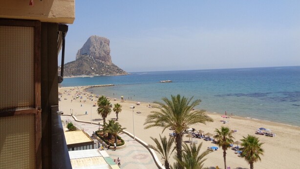 A beach with palm trees, a rocky outcrop, and a clear blue sky. - A47 CALPEMAR C 5º 19 (Calpe)