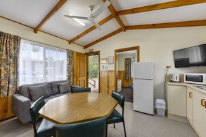 Una habitación con techo de madera, una mesa de comedor con sillas, un sofá, una zona de cocina con microondas y un televisor.