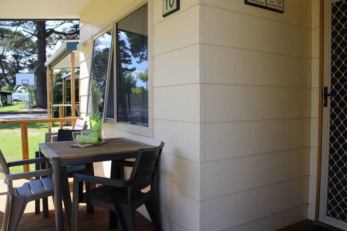 Quarto com mesa e cadeiras de madeira, janela com vista para o exterior e porta com placa de número.