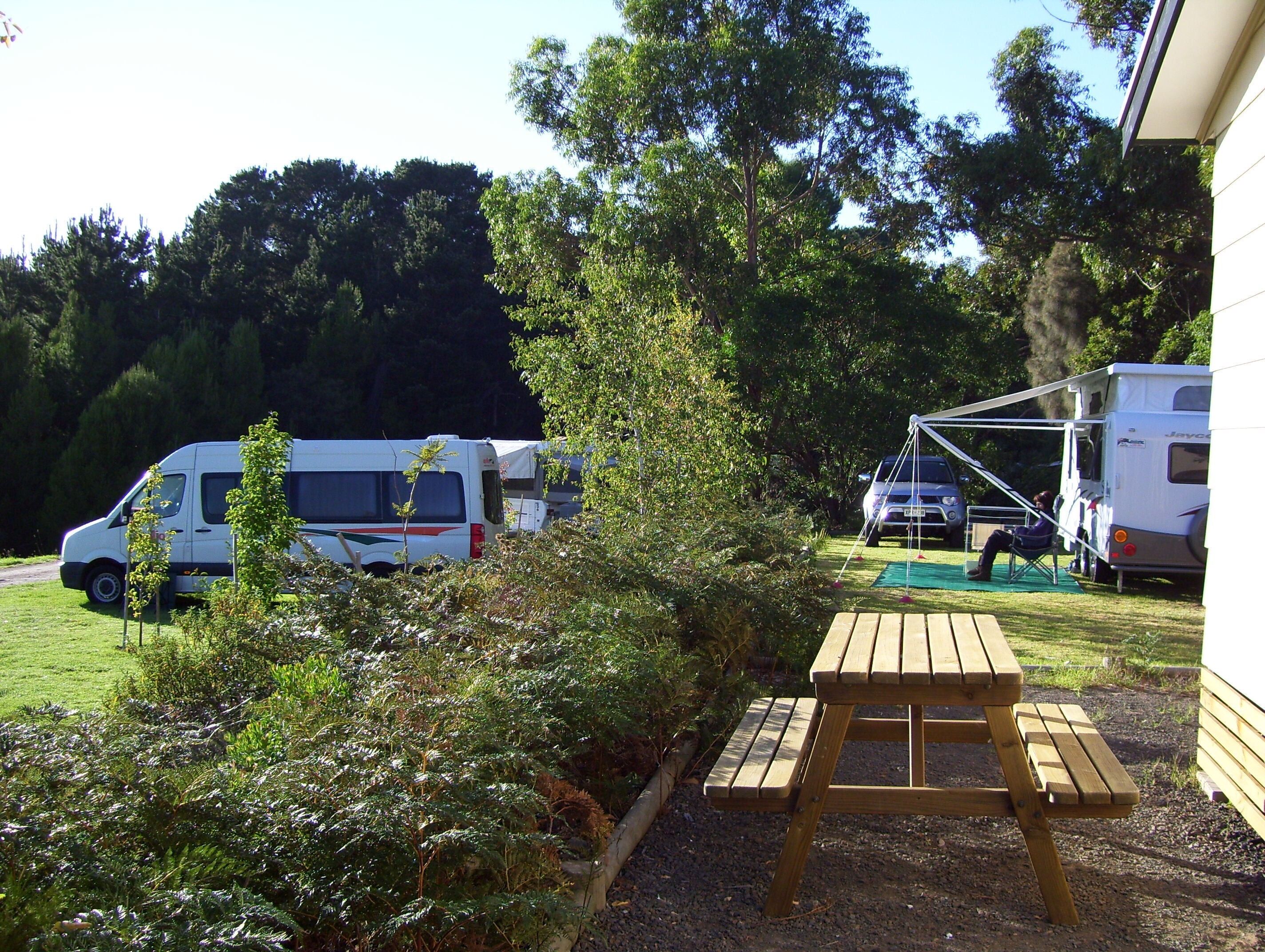 Un terrain de camping avec des emplacements pour camping-cars, une table de pique-nique et une végétation luxuriante.