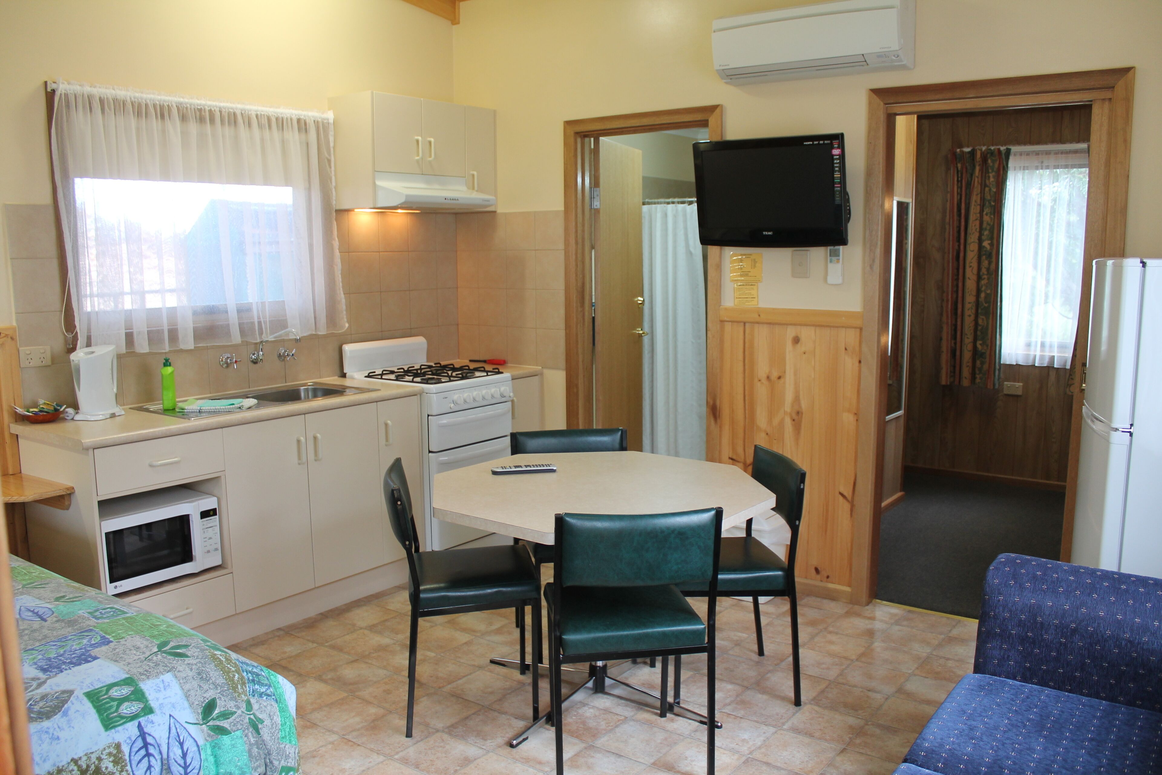 Una cocina compacta con mesa, sillas, microondas, cocina y televisor.