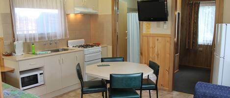Una cocina compacta con mesa, sillas, microondas, cocina y televisor.