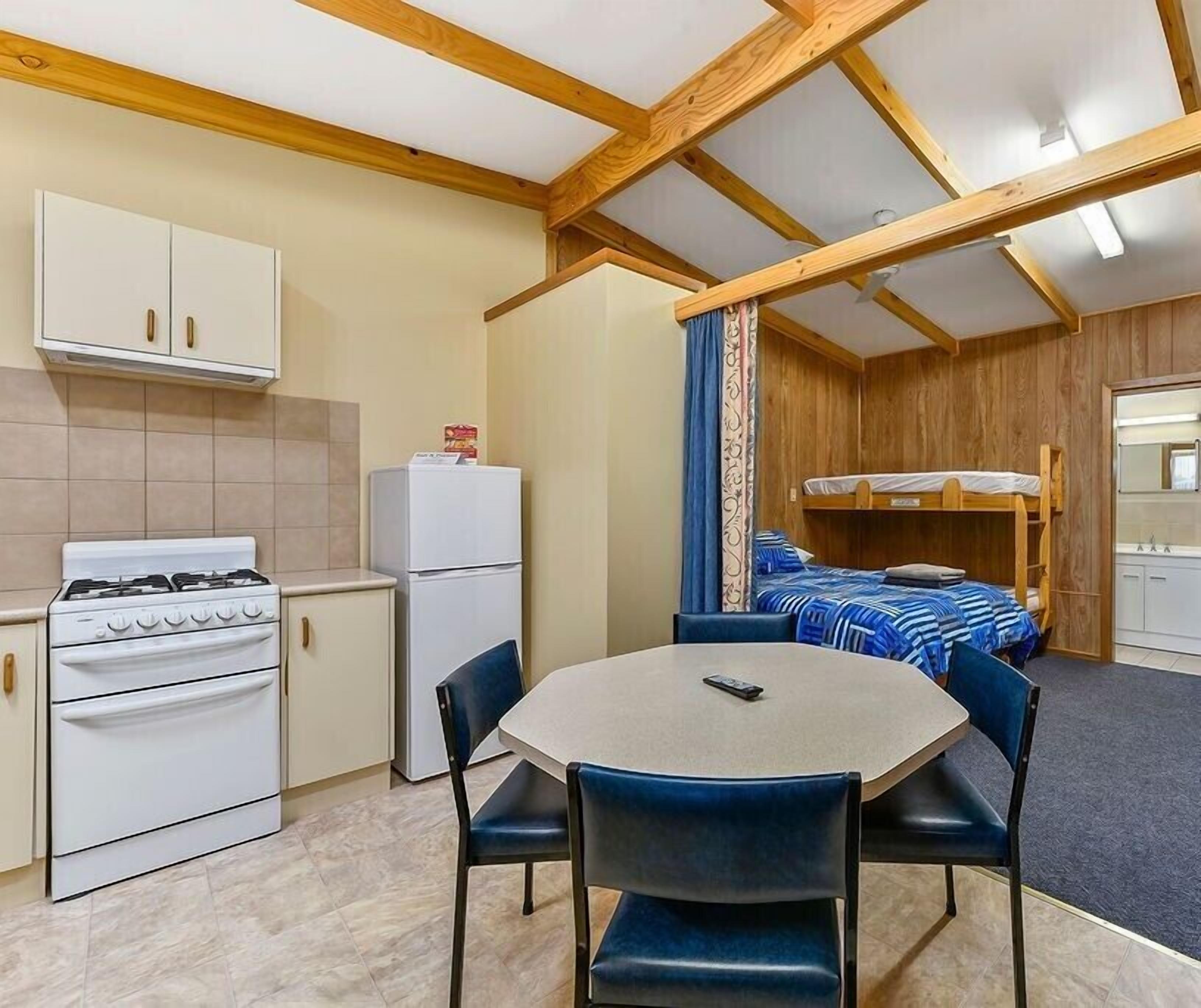 Une pièce compacte comprenant un coin cuisine, un lit superposé et une table à manger.