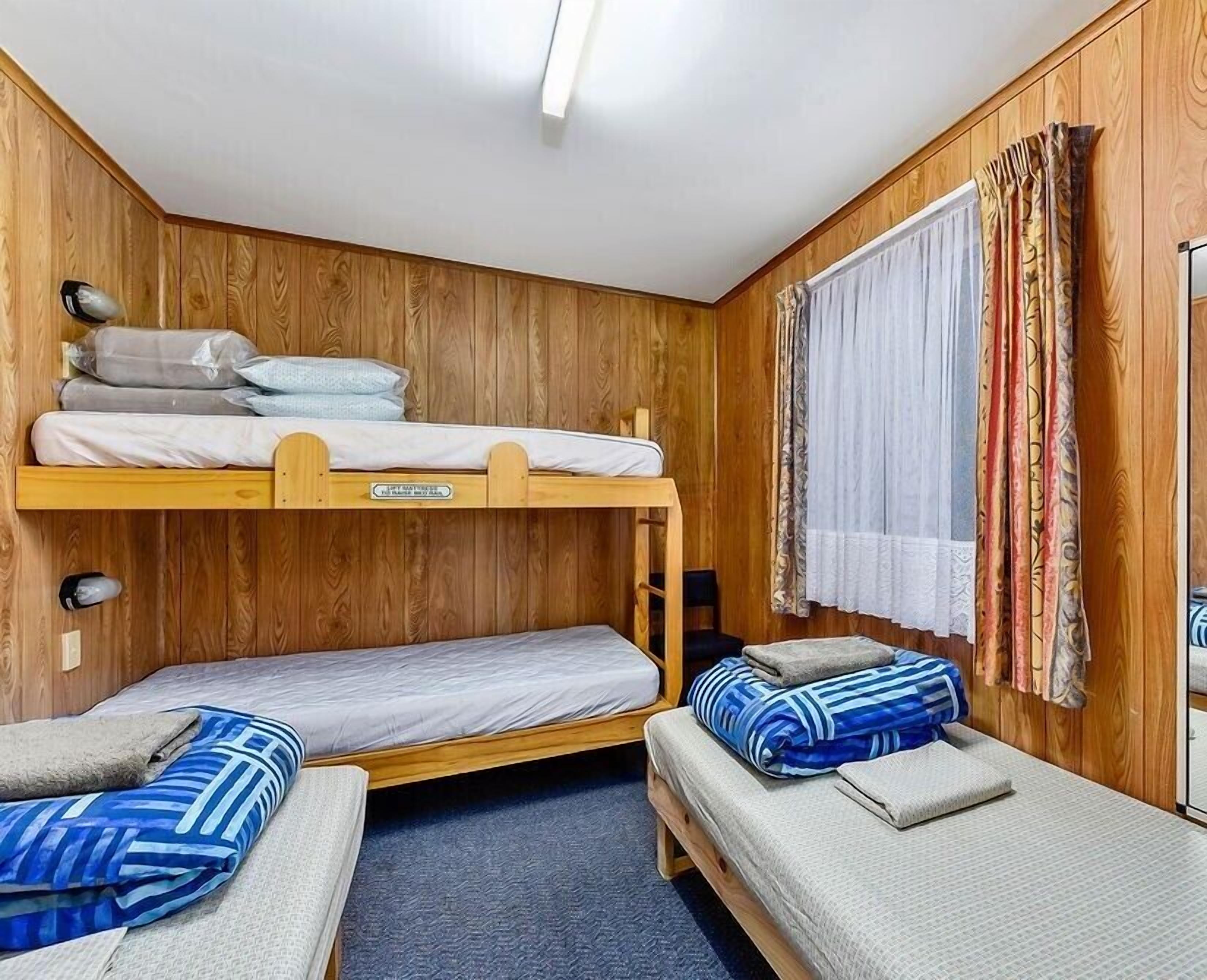 Habitación con literas, paredes de madera, una ventana con cortinas estampadas y un escritorio con silla.