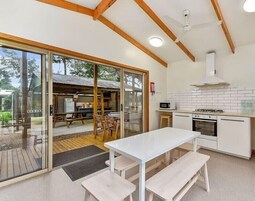 Una cocina moderna con gabinetes blancos, microondas y estufa. Hay una zona de comedor con una mesa y bancos.