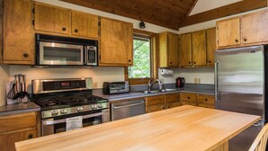 Cocina con gabinetes de madera, electrodomésticos de acero inoxidable, encimera de madera y ventana que deja entrar luz natural.