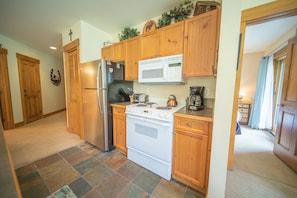 Kitchen area with central stove, refrigerator, and microwave, equipped with a coffee maker and kettle.
