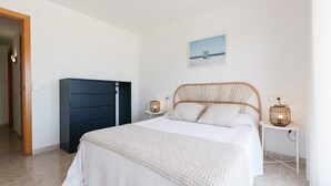 A bedroom with a bed, a wardrobe, a bedside table with a lamp, and a picture on the wall. - Beachfront apartment perfect for families · UHC ARCO DEL SOL 277 (Hospitalet de L´Infant)