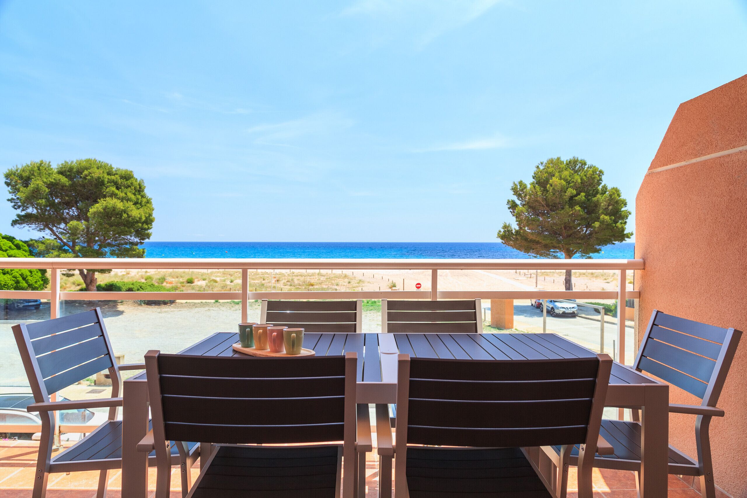 Eine Terrasse mit Tisch und Stühlen mit Blick auf einen Strand und das Meer.
