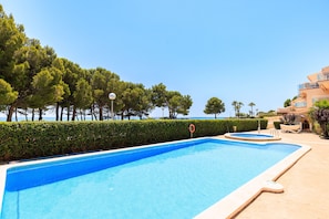 Une piscine offrant une vue dégagée sur la mer, entourée d’arbres et bordée d’un bâtiment doté de balcons.
