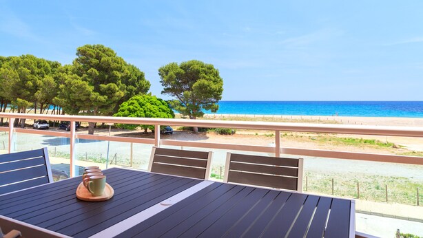 A balcony with a view of the sea, a table with chairs, and a wooden coffee table. - Beachfront apartment perfect for families · UHC ARCO DEL SOL 277 (Hospitalet de L´Infant)