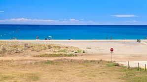 A beach with a clear blue sky, a sandy shore, and a few people and umbrellas. - Beachfront apartment perfect for families · UHC ARCO DEL SOL 277 (Hospitalet de L´Infant)