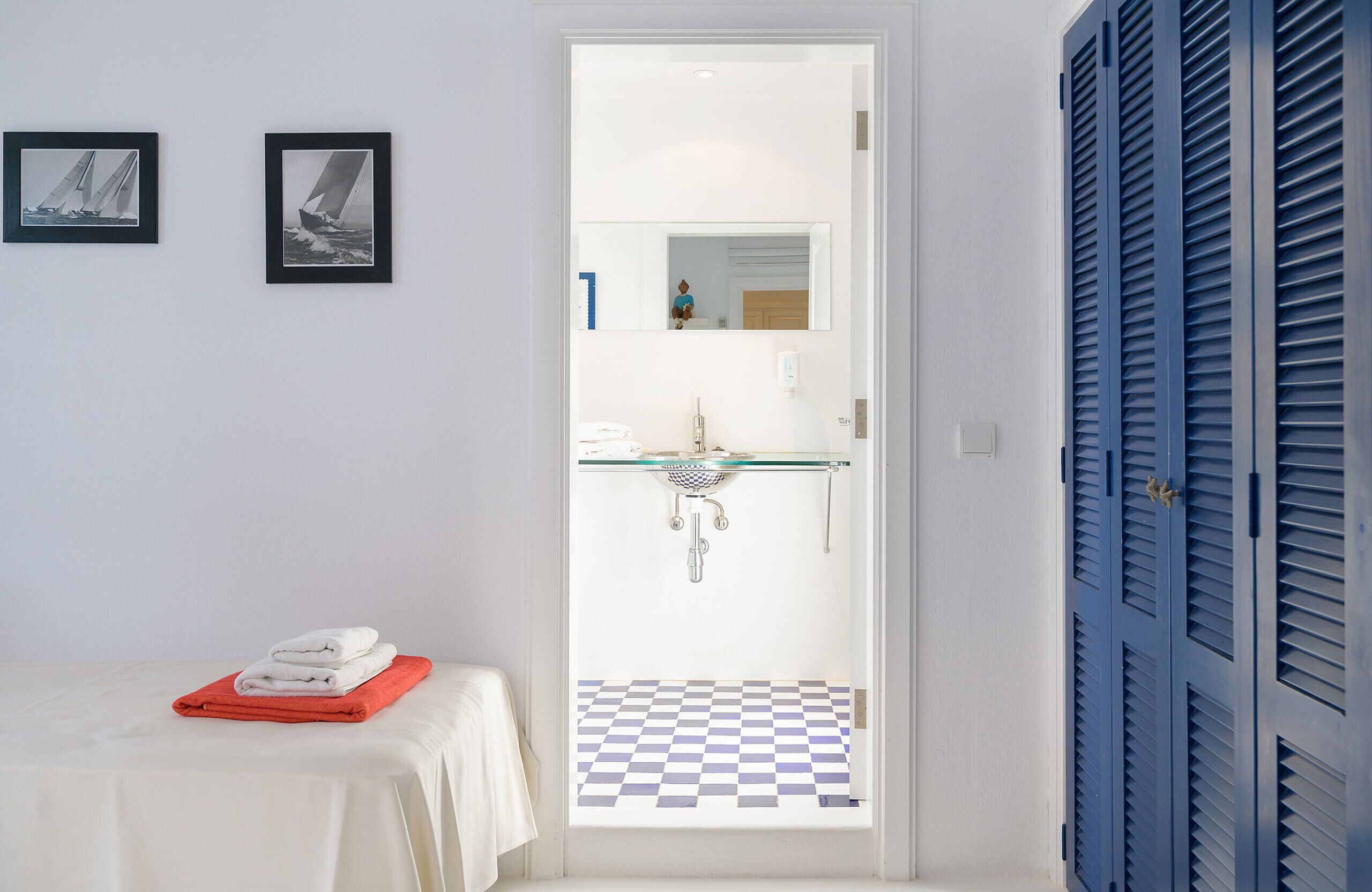 A bathroom with a checkered floor, a sink, and a mirror. There are towels on a table and a door with blue shutters.