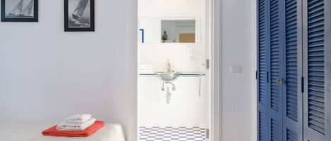A bathroom with a checkered floor, a sink, and a mirror. There are towels on a table and a door with blue shutters.