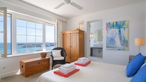 A hotel room with a bed, a wooden dresser, a chair, a window with a view of the sea, and a painting on the wall. - Casa Lola, Sea Front Apartment in Playa Blanca (Playa Blanca)