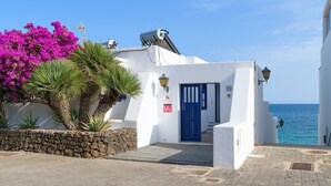 A white building with a blue door, a stone wall, and a view of the sea. - Casa Lola, Sea Front Apartment in Playa Blanca (Playa Blanca)