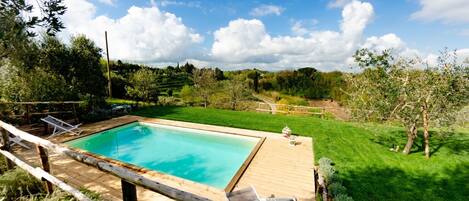 A rectangular swimming pool with a wooden deck and lounge chairs.
