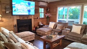 Una sala de estar acogedora con chimenea, sofás cómodos, un televisor de pantalla plana y ventanas amplias.