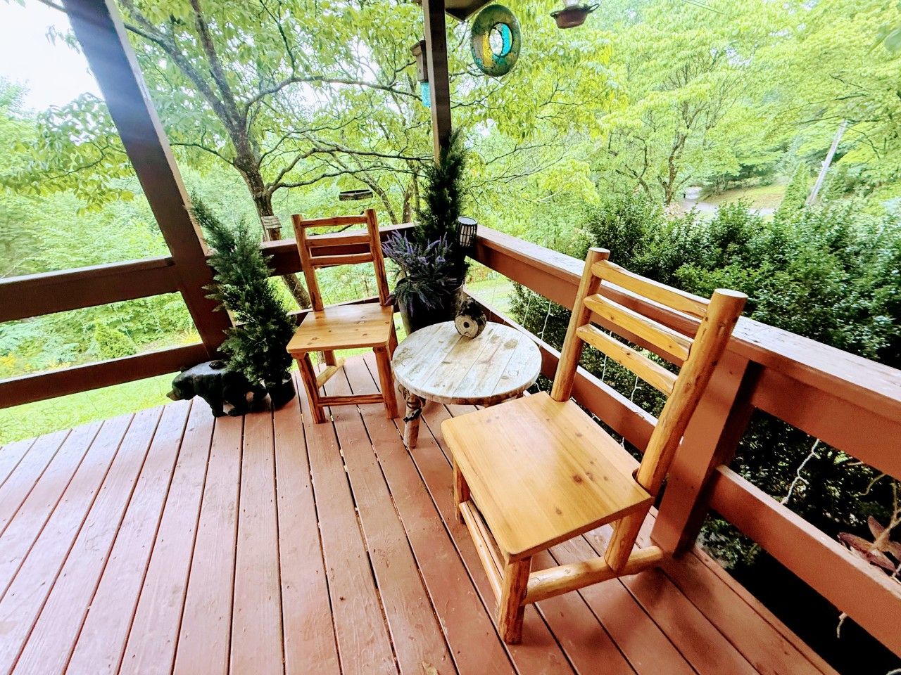 A wooden deck with a bench and a table, surrounded by greenery.