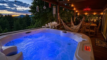 A hot tub with a blue light, surrounded by wooden furniture and string lights.