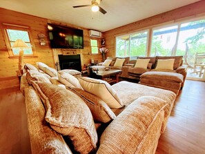 A cozy living room with a fireplace, a television, and a large window providing natural light. - Mountain View Cabin Hot Tub,Wifi,Casino (Whittier)