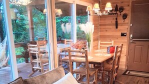 A cozy cabin interior with a wooden dining table, chairs, a sofa, and a large window overlooking a deck. - Mountain View Cabin Hot Tub,Wifi,Casino (Whittier)
