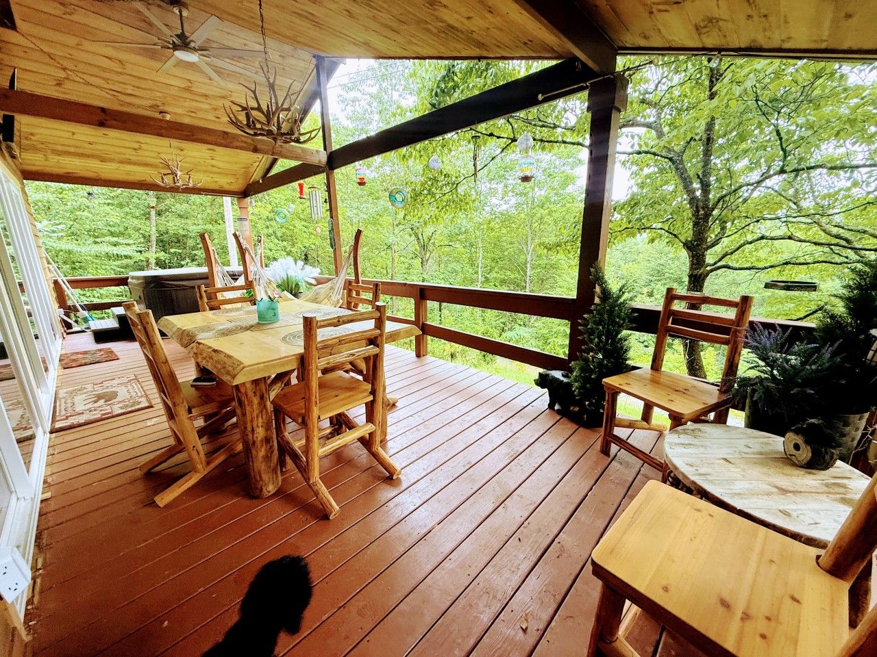 Een houten terras met een tafel en stoelen, omringd door een reling, met uitzicht op een bebost gebied.
