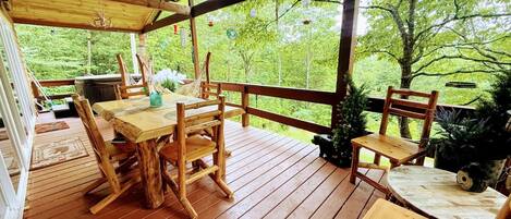 Een houten terras met een tafel en stoelen, omringd door een reling, met uitzicht op een bebost gebied.