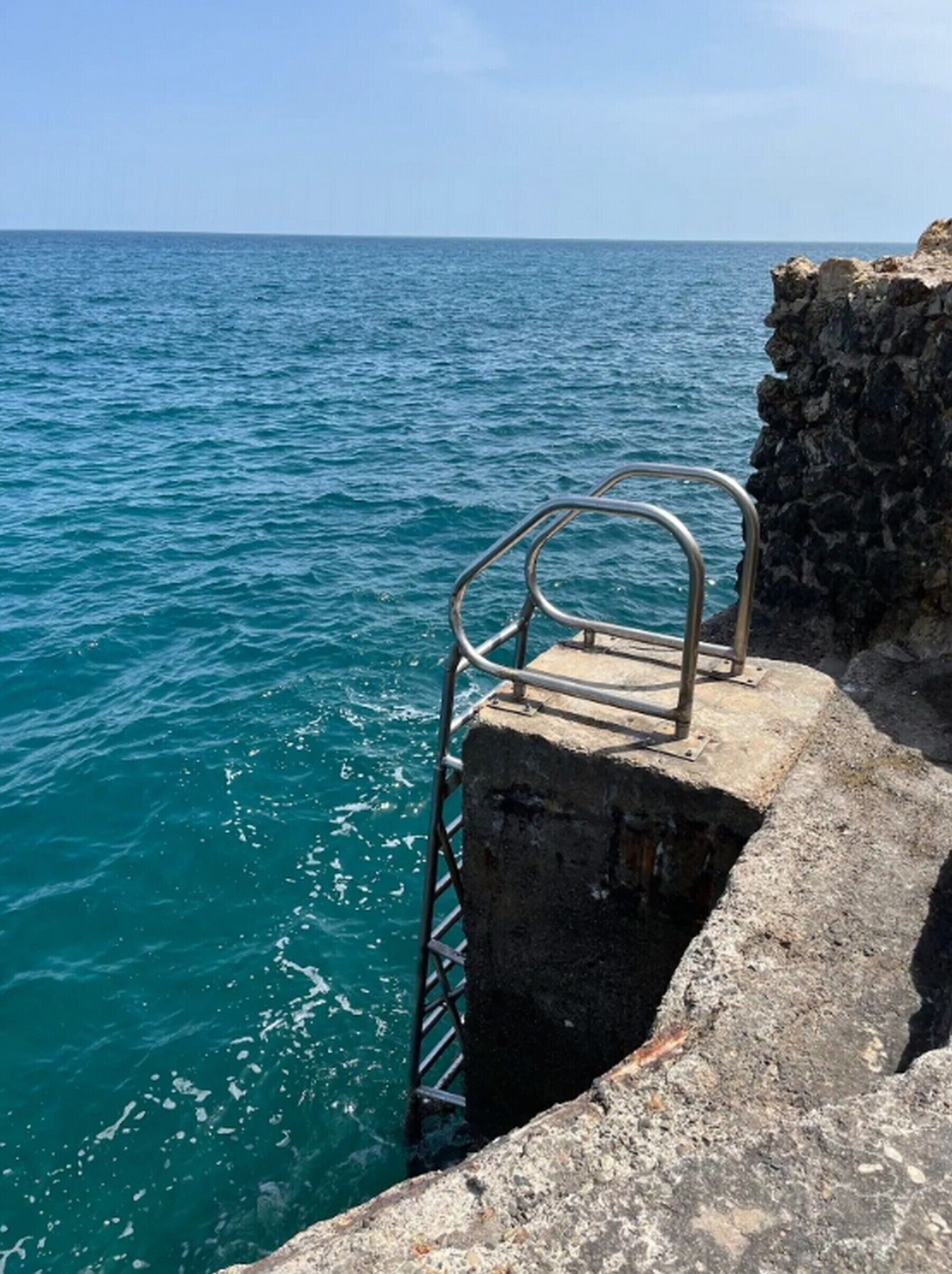 Un pilier en béton avec une échelle métallique qui descend vers la mer.