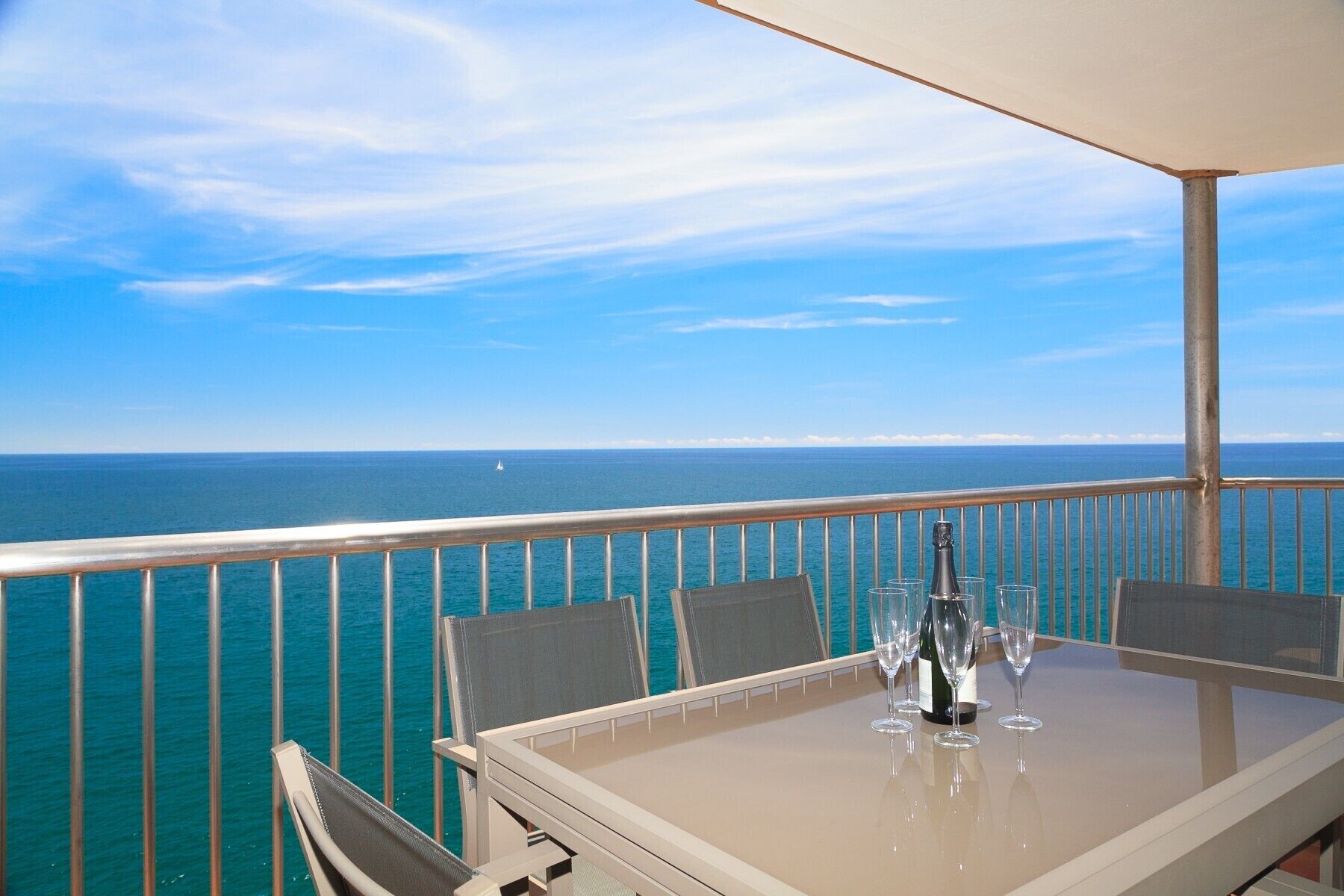 Uma mesa com quatro cadeiras e uma garrafa de vinho em uma varanda com vista para o oceano.