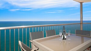 A table with four chairs and a bottle of wine on a balcony overlooking the ocean.