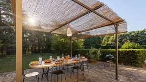 An outdoor patio with a round table set for dining, surrounded by chairs, and a grill in the background. - Villa in Il Passaggio with 5 bedrooms sleeps 10 (Il Passaggio)
