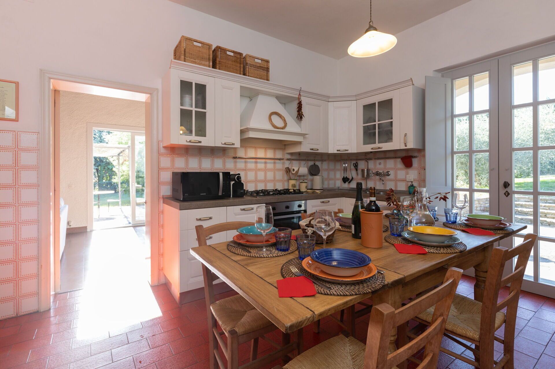 A spacious kitchen with white cabinets, a wooden dining table, and a view of the garden through large windows.